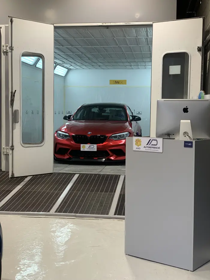 Cabina de pintura oberta amb un cotxe vermell a dins i el taulell de recepció al davant