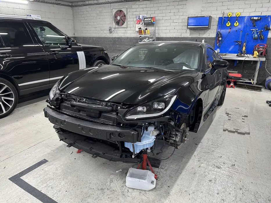 Cotxe negre amb el frontal desmuntat per reparar la xapa